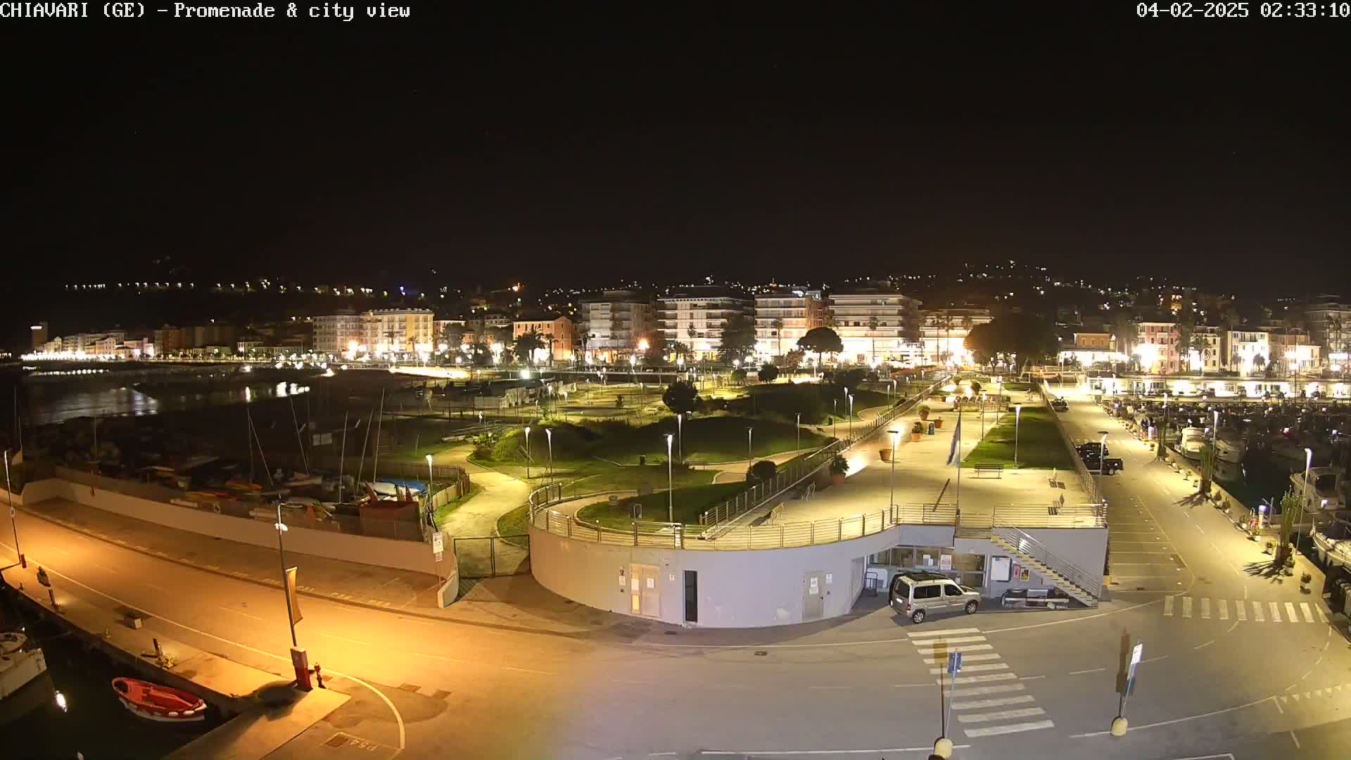 A nighttime view of a city's waterfront promenade and harbor, with its buildings, park, and boats illuminated under a clear, dark sky.