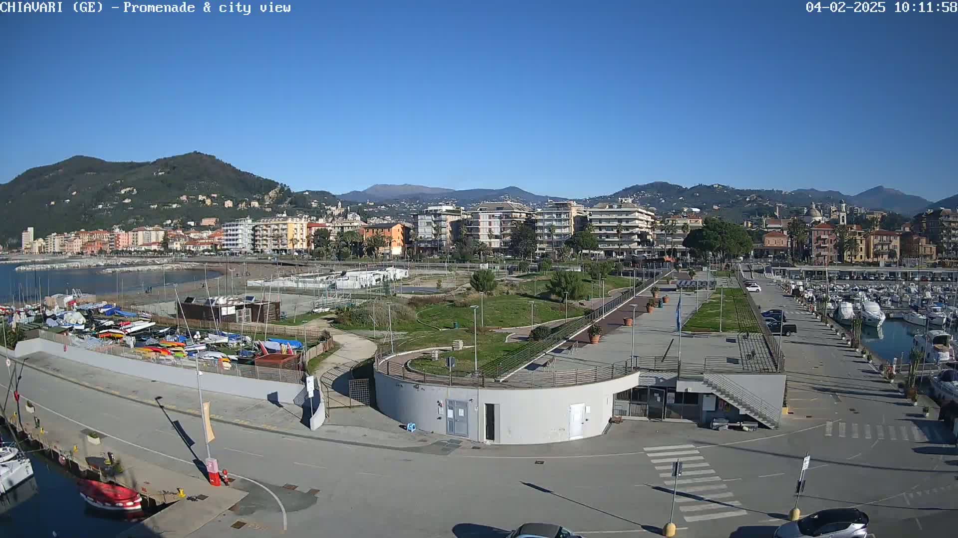 A seaside town with a marina, promenade, and park is visible under a clear blue sky.