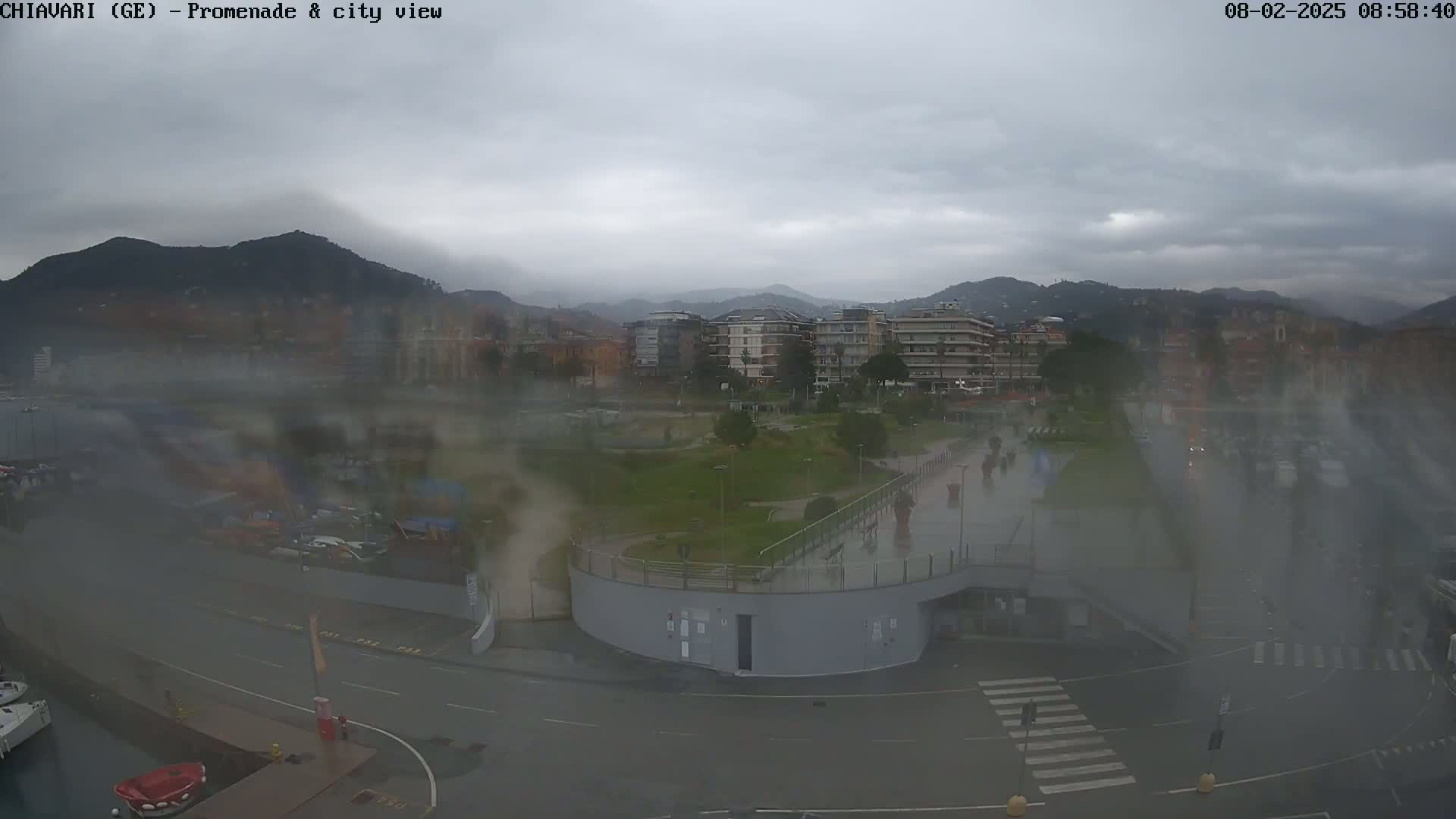 A rain-swept city promenade and harbor, with a background of hills and buildings under a cloudy sky.