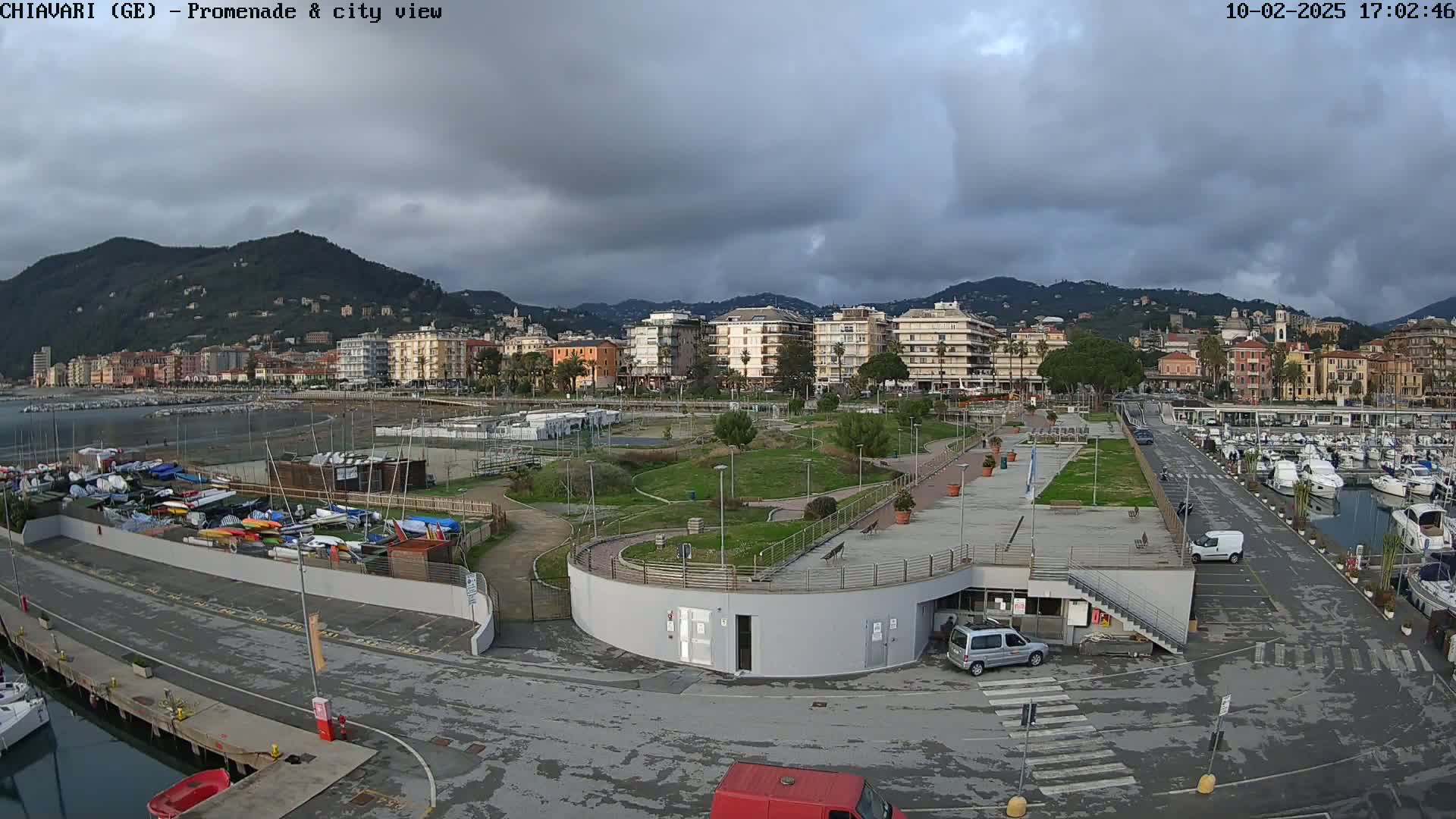 A coastal city with a marina and promenade is shown under a cloudy sky.