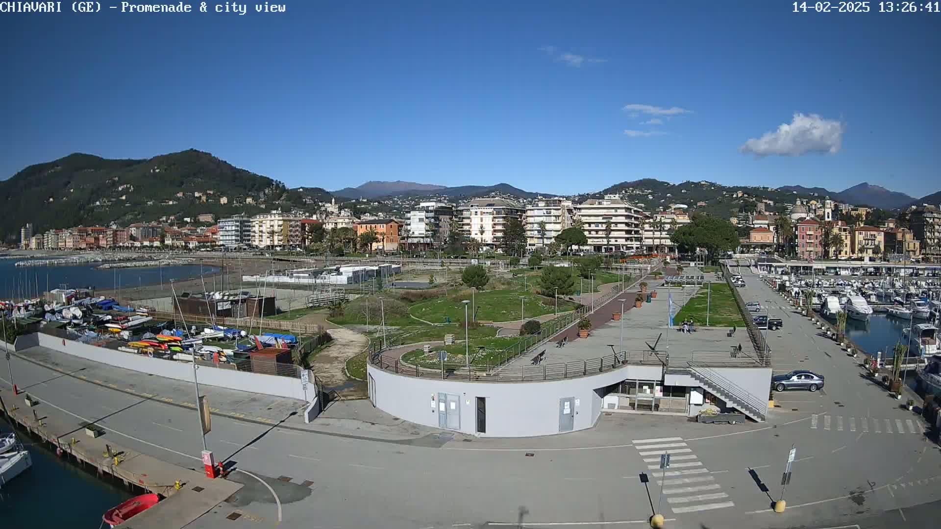 A sunny day reveals a coastal city with a marina filled with boats, a park, and buildings nestled against a backdrop of hills.