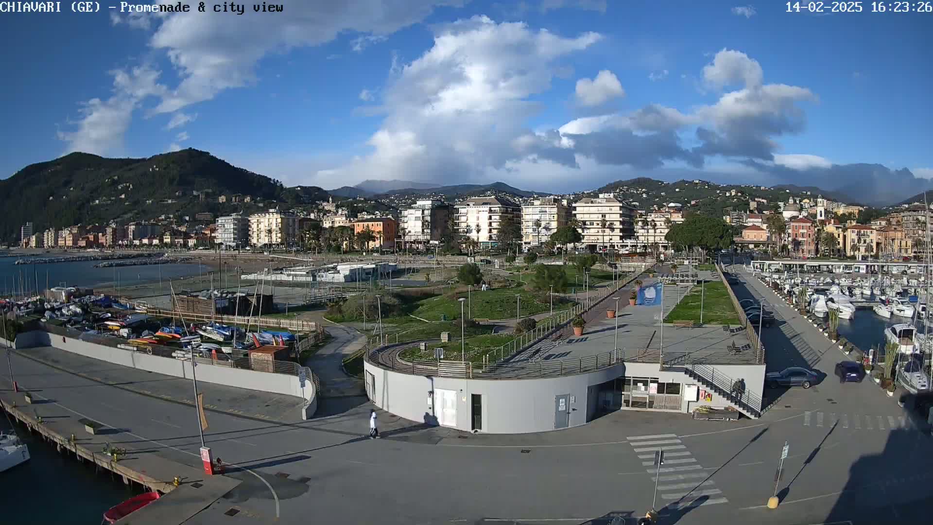A coastal town with a marina, promenade, and green spaces under a partly cloudy sky.