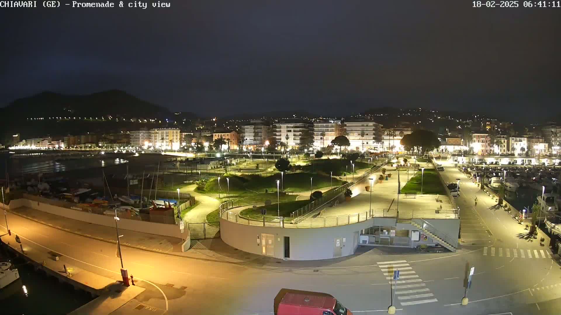 A nighttime aerial view of a harbor promenade and city, illuminated by streetlights, with a mostly clear sky.