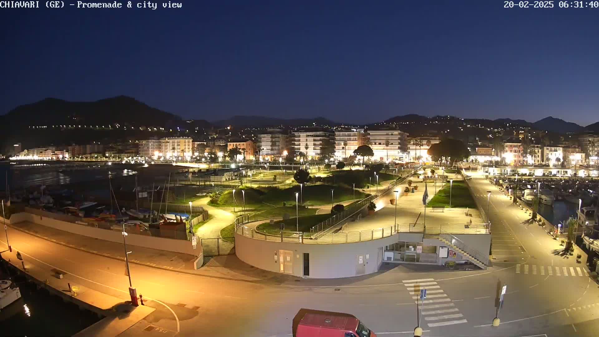 A nighttime, illuminated view of a harbor, promenade, and city nestled against a dark mountain range under a clear, dark sky.