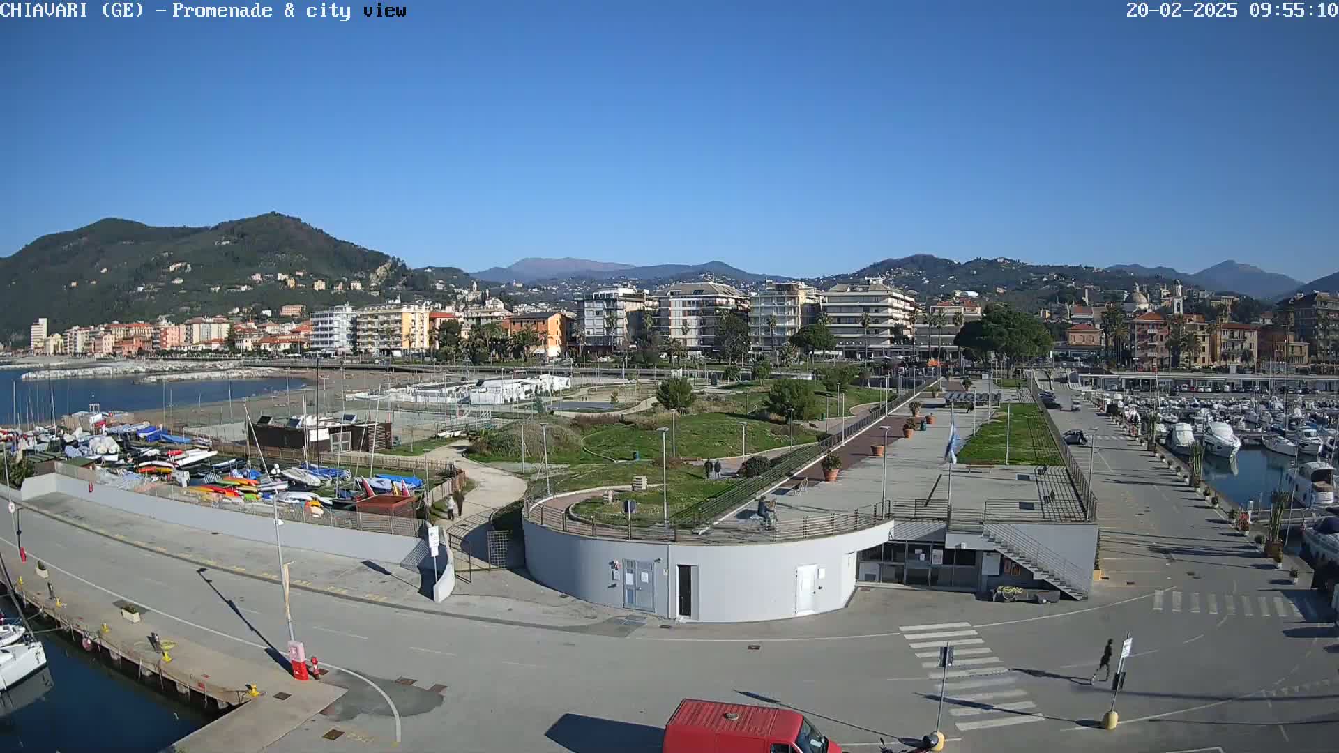 A seaside town with a marina, park, and buildings stretches along a coastline under a clear blue sky.