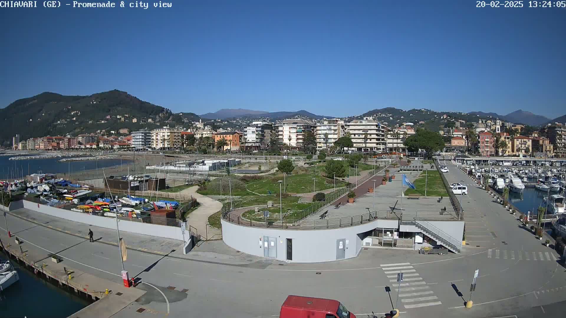 A seaside town with a marina, promenade, and park is viewed under sunny skies.
