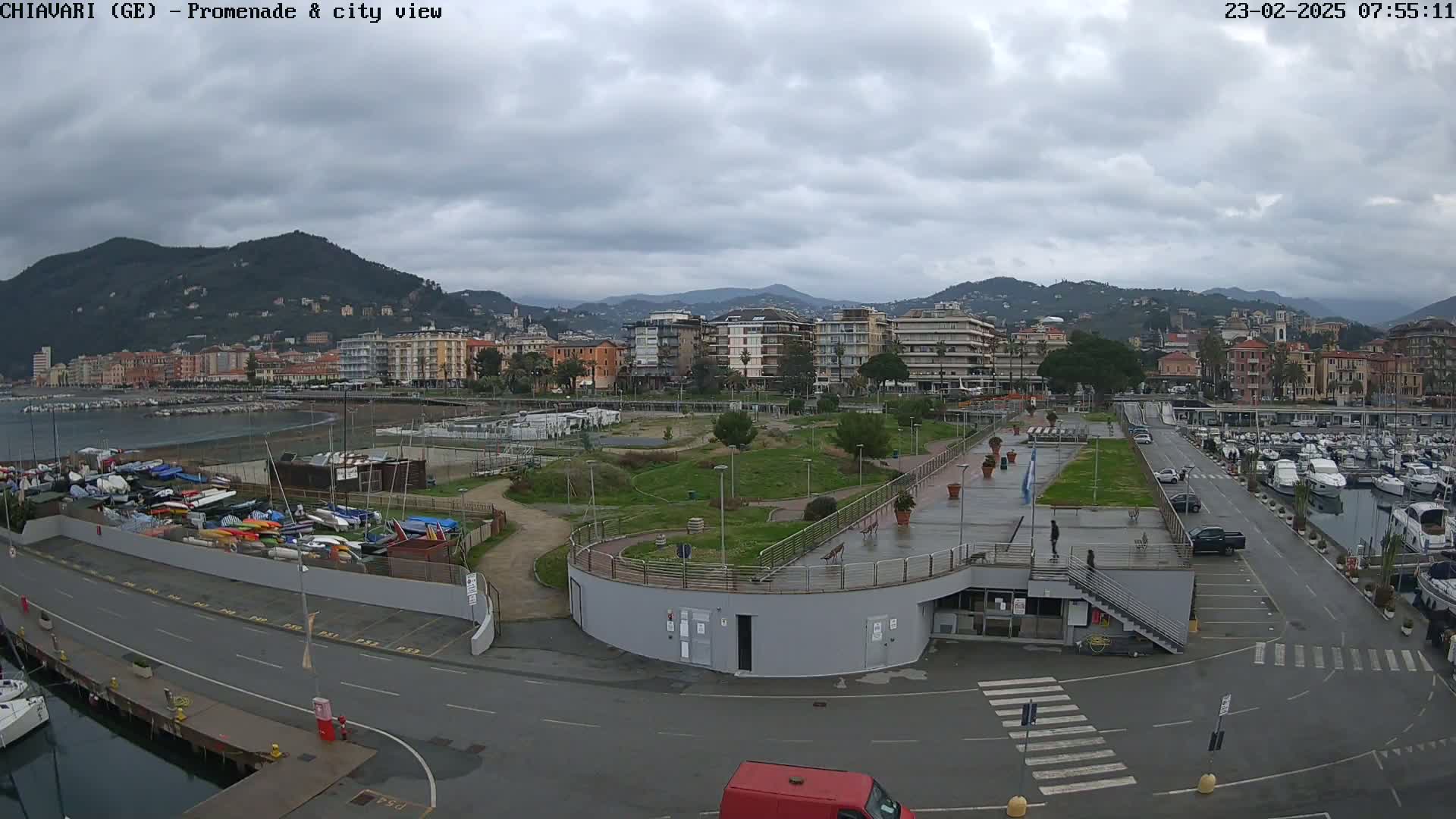 A coastal city with a promenade, marina, and park is visible under an overcast sky.