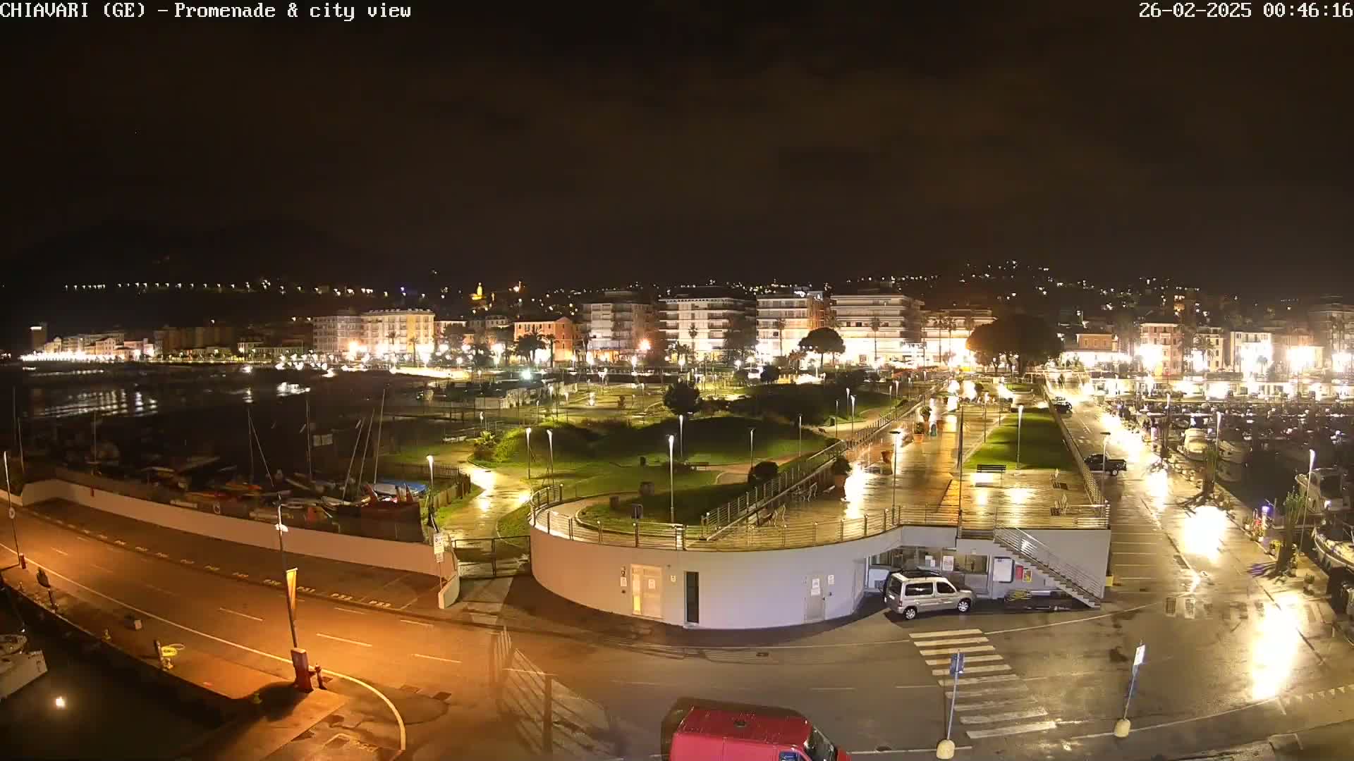 A rain-slicked nighttime view of a coastal town's illuminated promenade, harbor, and buildings.