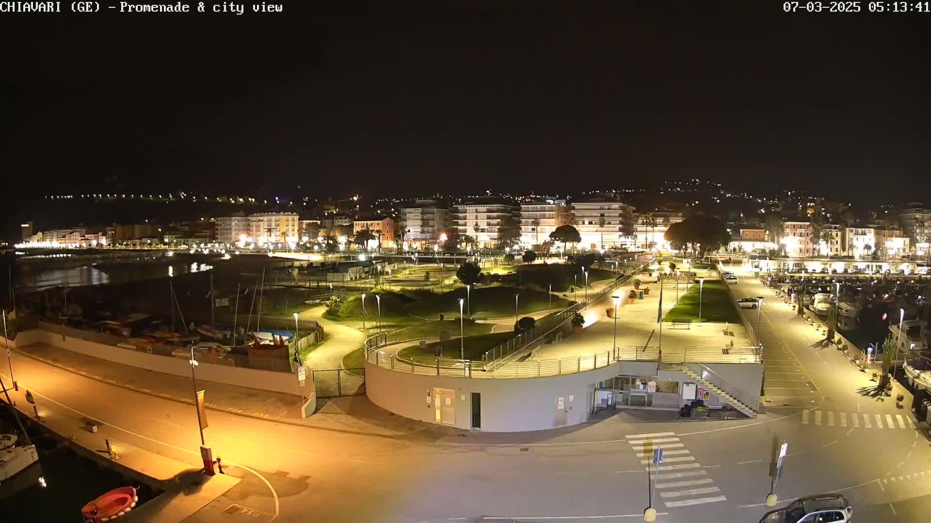 A nighttime view of a city's illuminated waterfront promenade and marina, featuring a park and buildings.