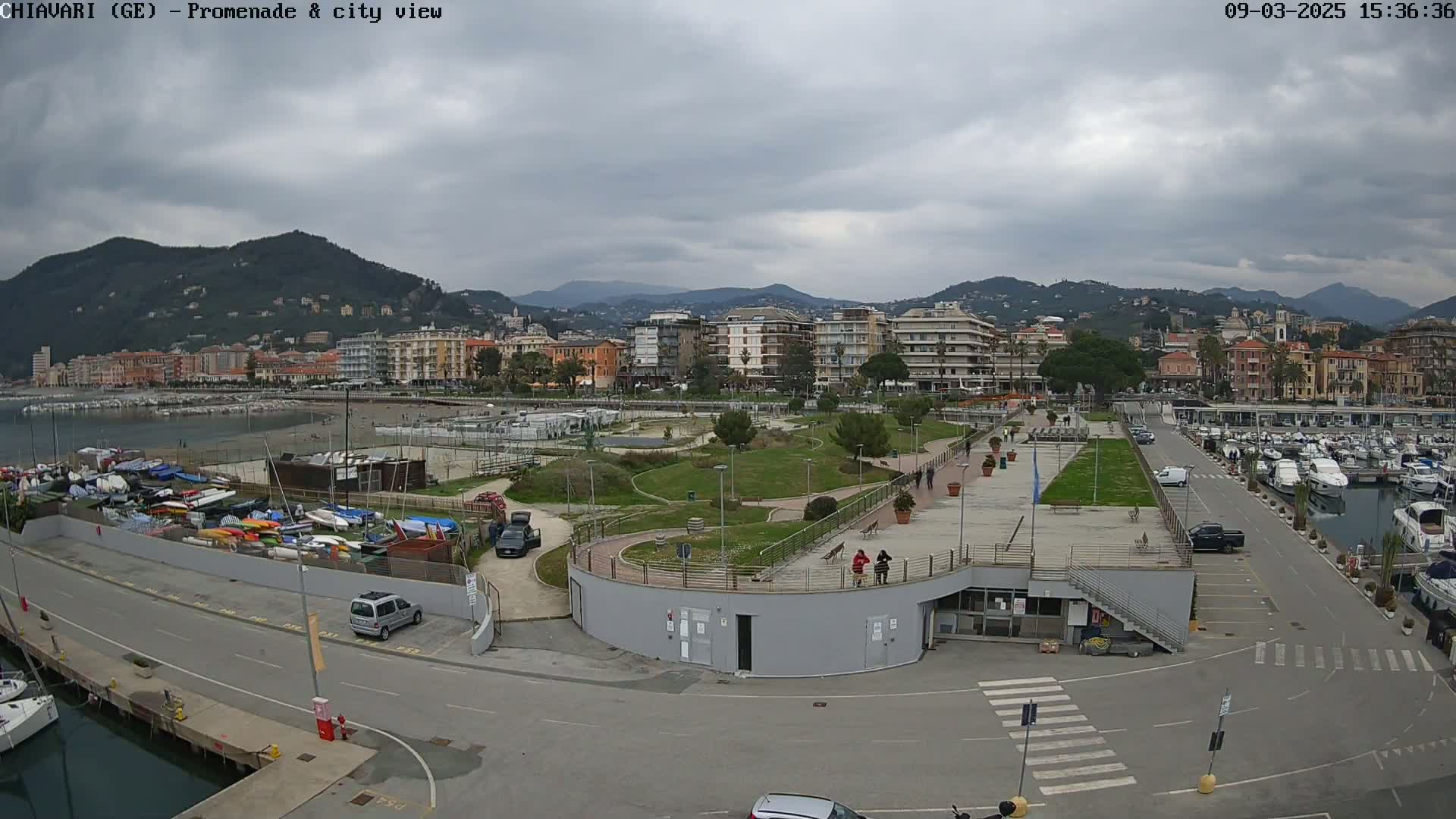 A seaside town with a promenade, park, and marina under a cloudy sky.
