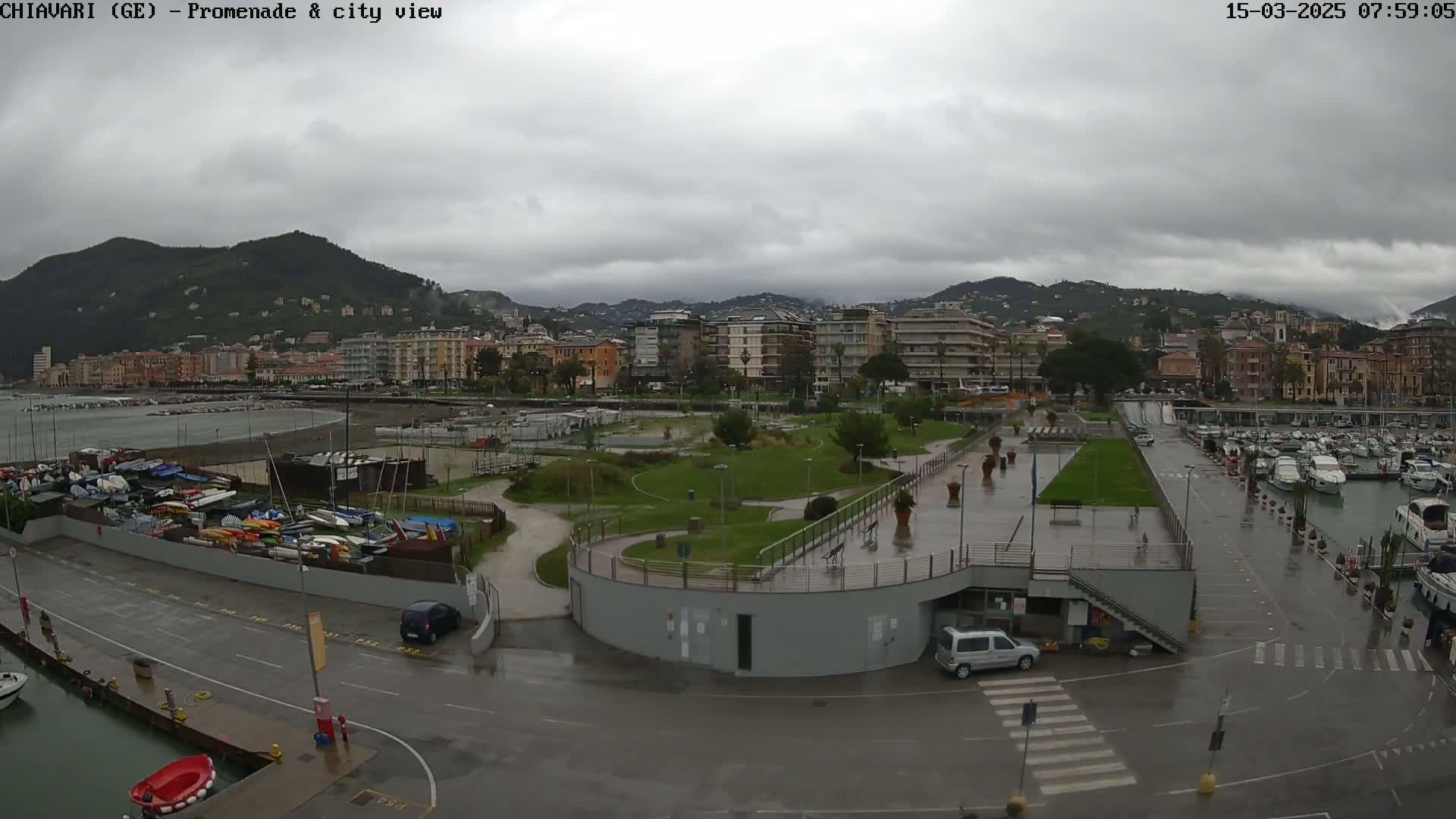 A wet promenade and harbor overlook a city nestled between hills under a cloudy sky.