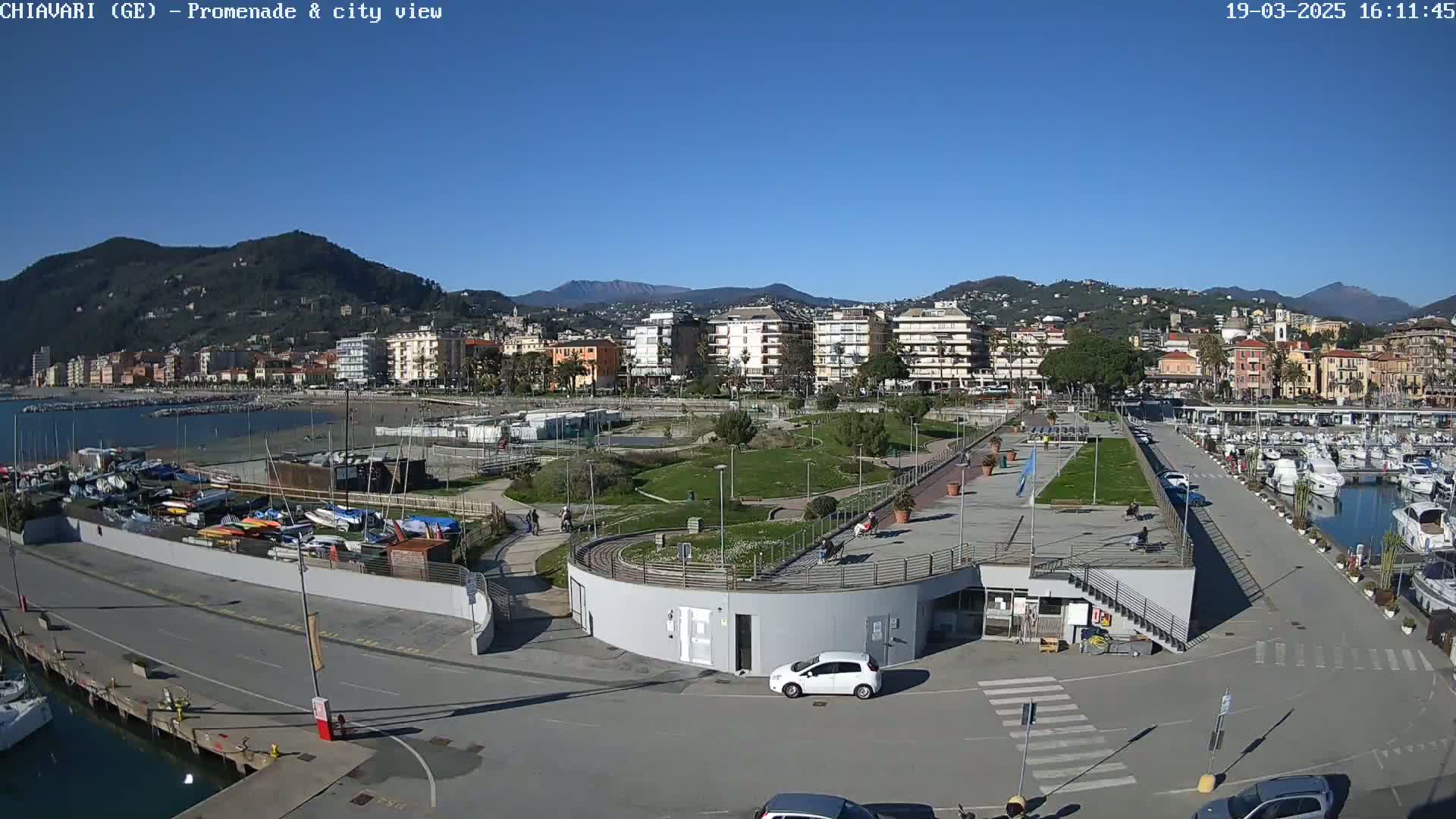 A waterfront promenade and city with a marina filled with boats under a clear blue sky.