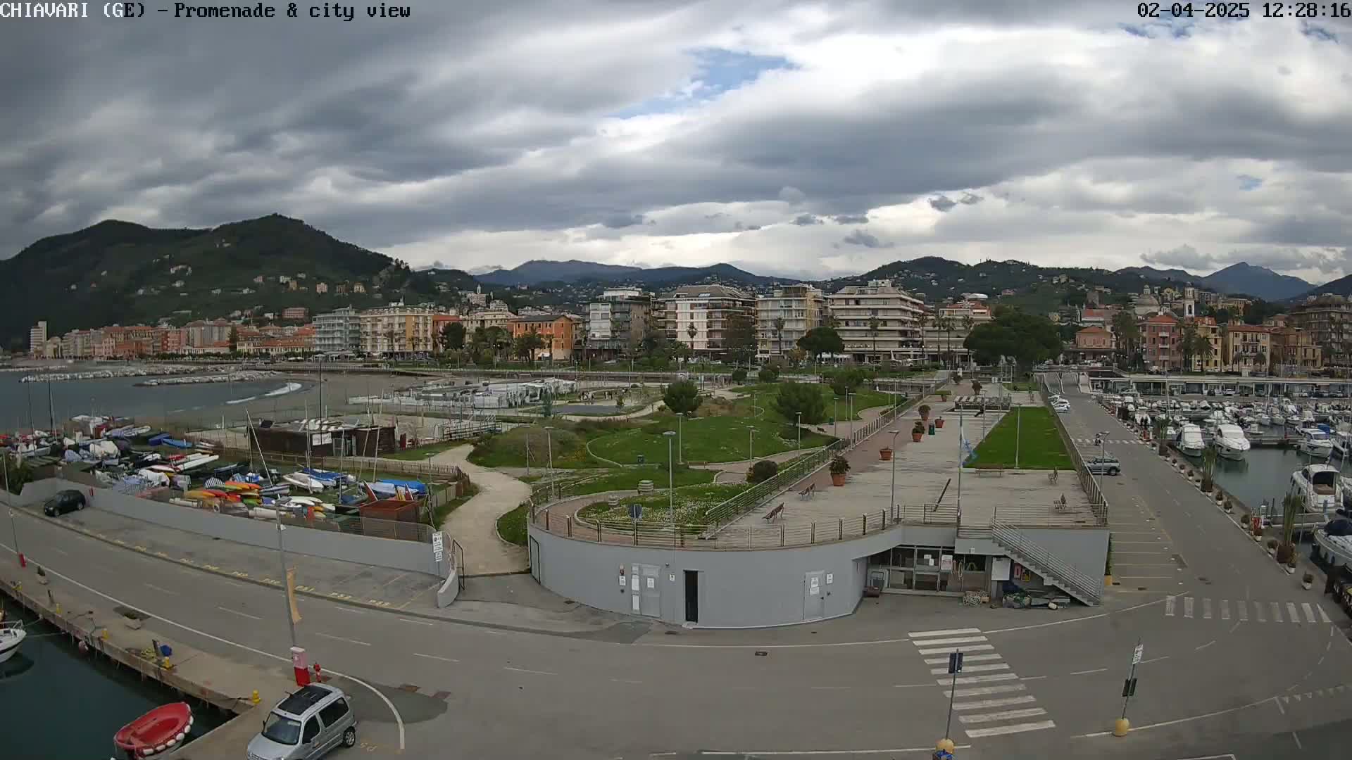 A coastal city with a marina and promenade is viewed under a cloudy sky.