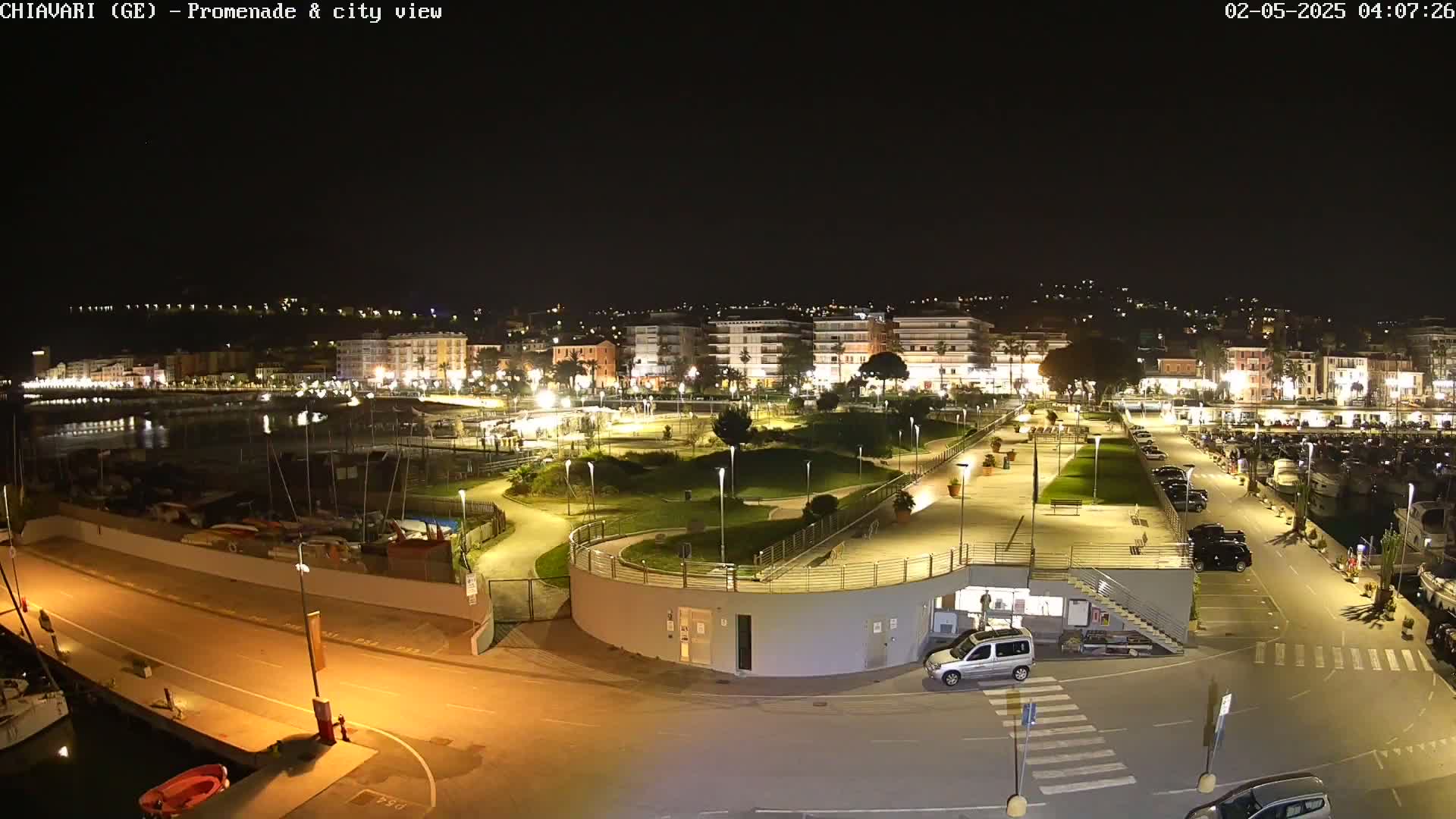 A nighttime aerial view of a harbor town with a well-lit promenade, park, and marina.
