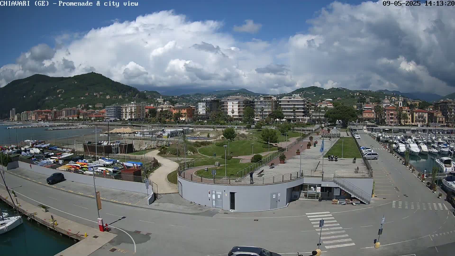 A coastal city with a marina and a promenade is shown under a partly cloudy sky.