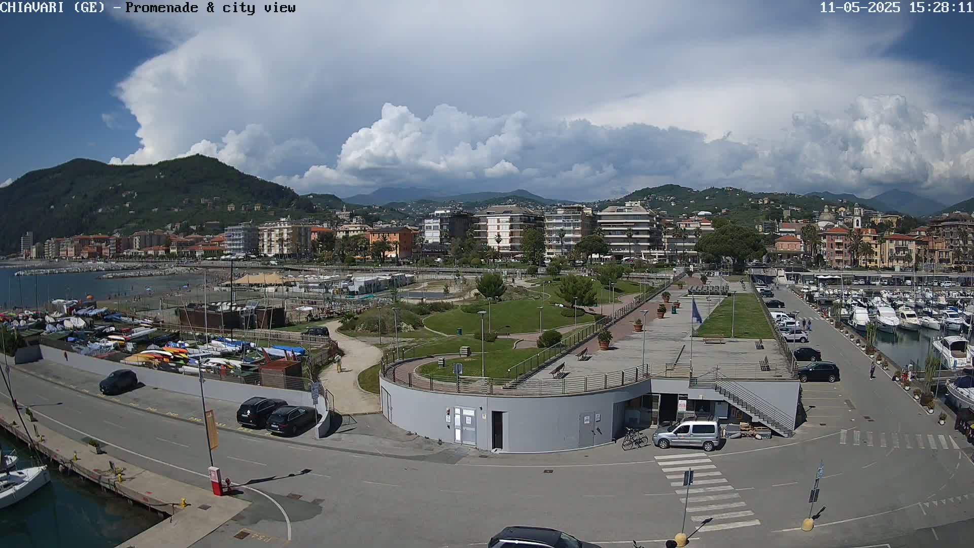 A coastal town with a marina, a promenade, and a park is visible under a partly cloudy sky.