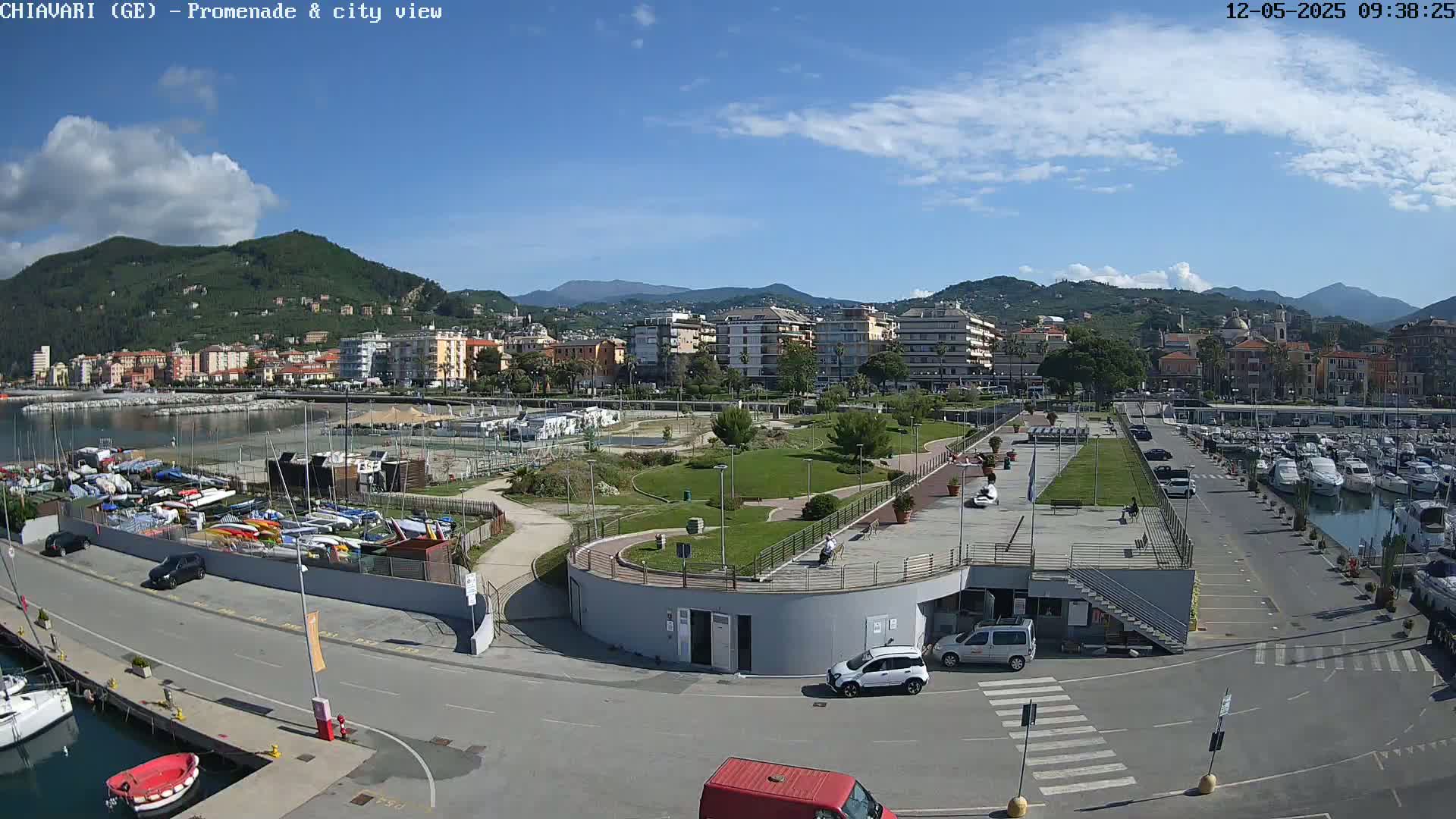 A sunny day overlooking a harbor filled with boats, a park, and a coastal town nestled against mountains.