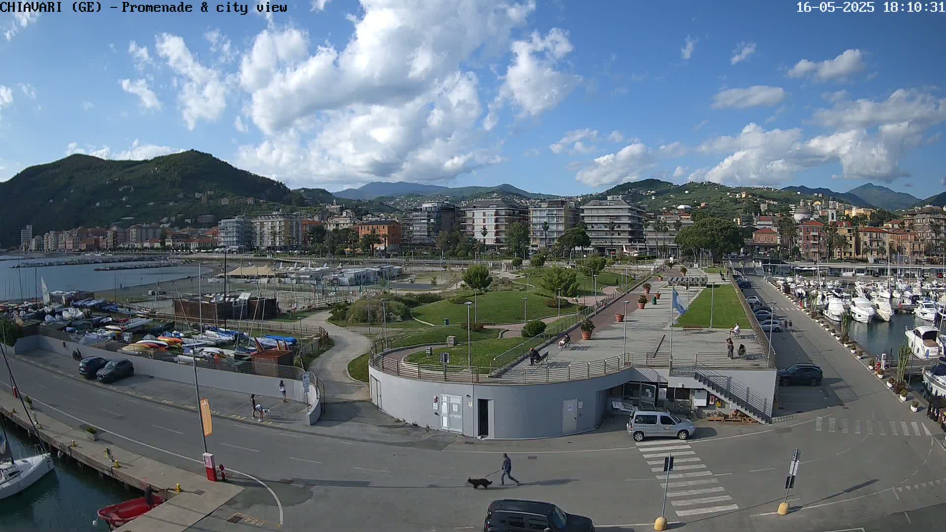 A seaside town with a marina, promenade, and park is visible under a partly cloudy sky.