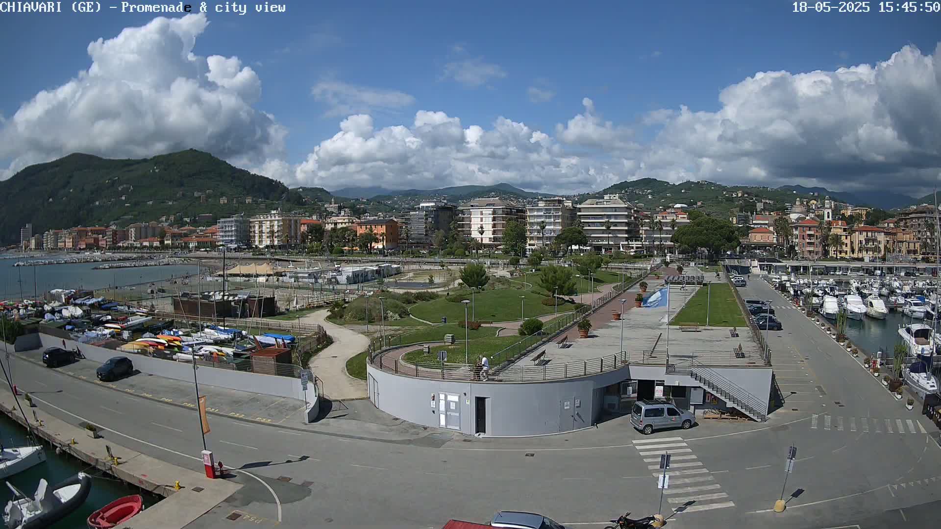 A coastal city with a harbor full of boats, a park, and buildings, under a partly cloudy sky.