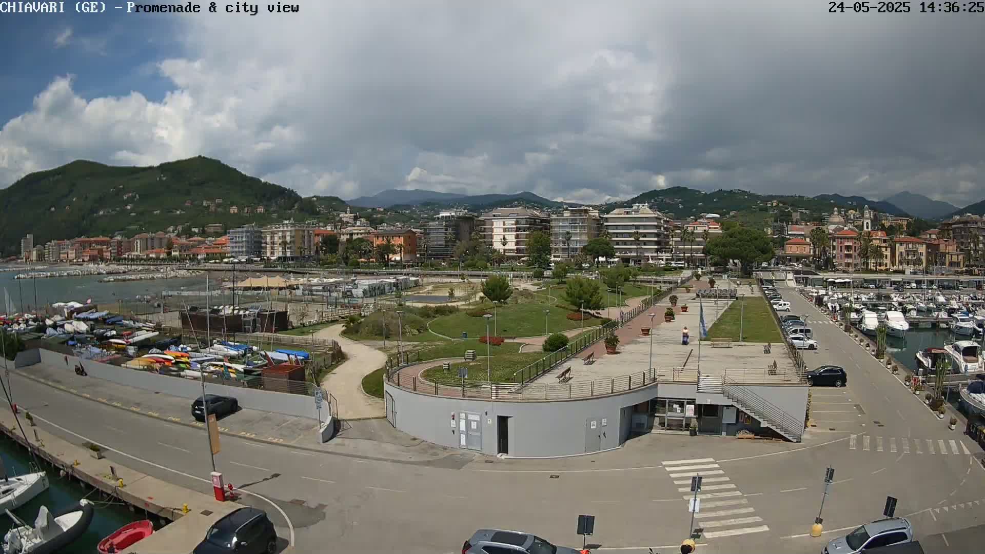 A coastal city with a marina, park, and residential buildings is seen under a partly cloudy sky.