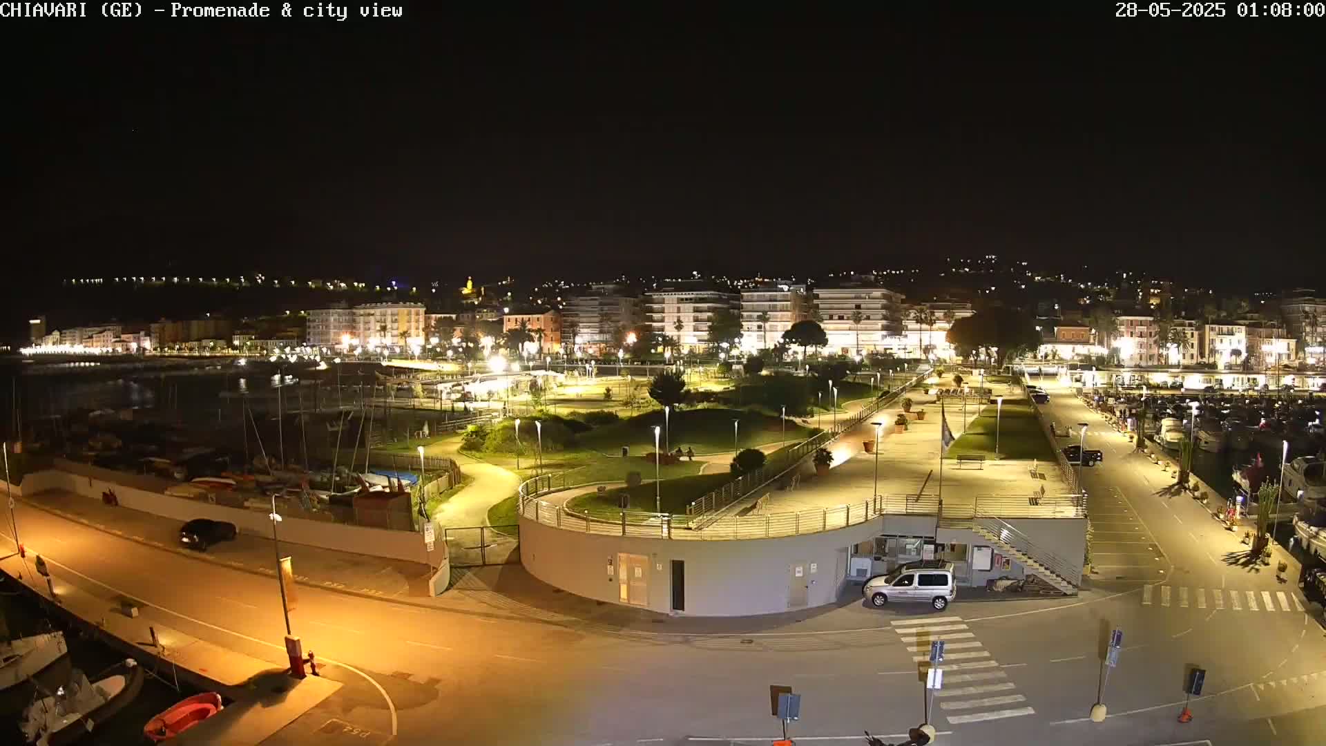 A nighttime view of a city's waterfront promenade, marina, and buildings illuminated by artificial light.