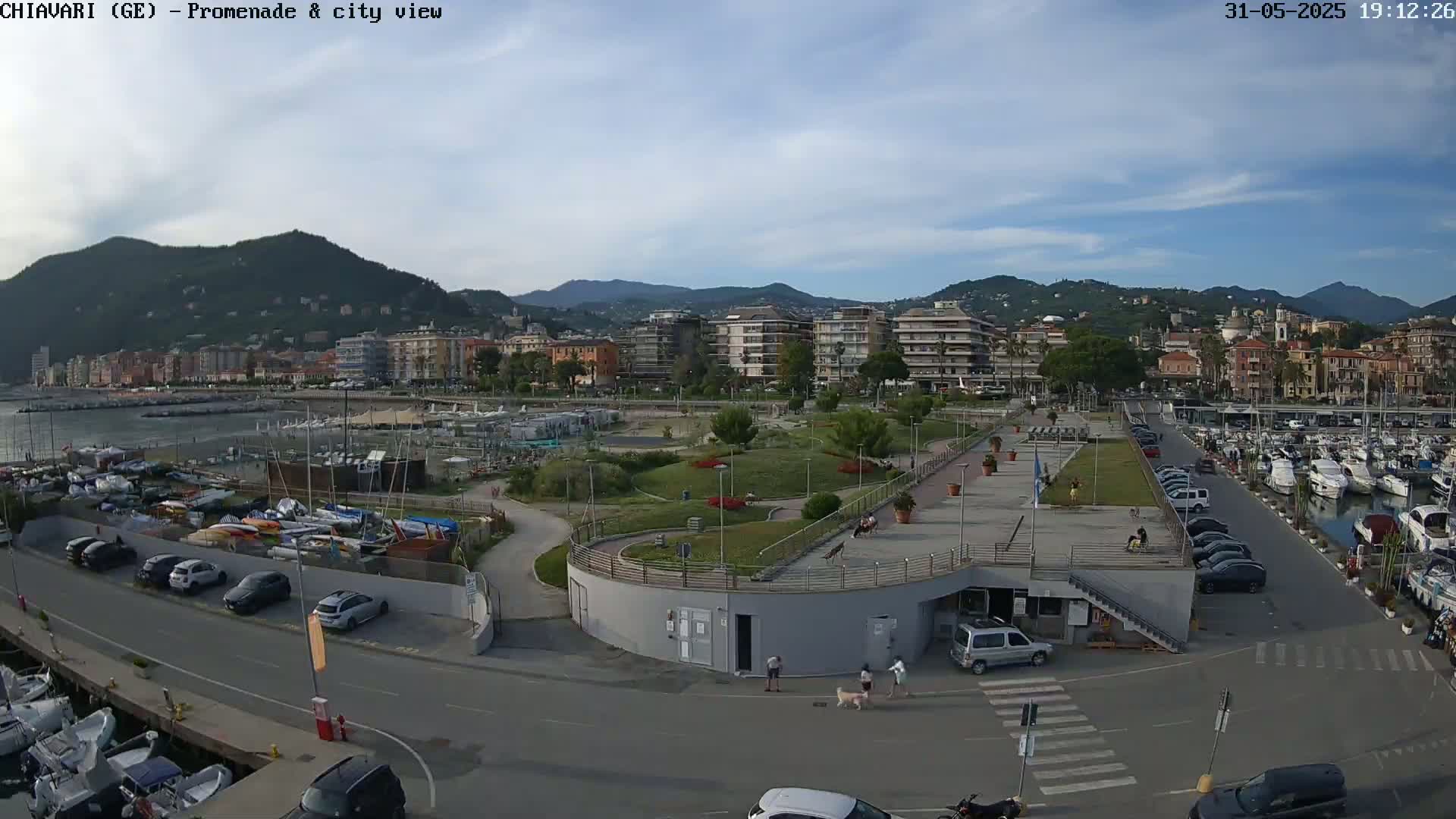 A coastal city with a marina and promenade, under a partly cloudy sky.