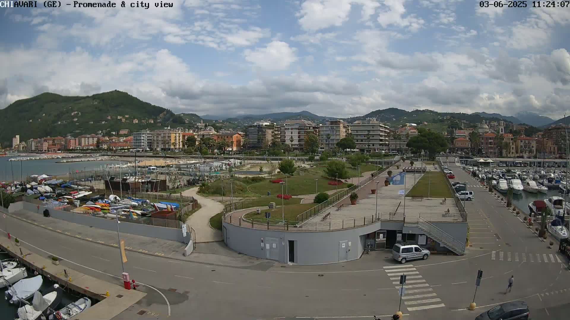 A coastal city with a marina and promenade is shown under partly cloudy skies, with mountains visible in the background.