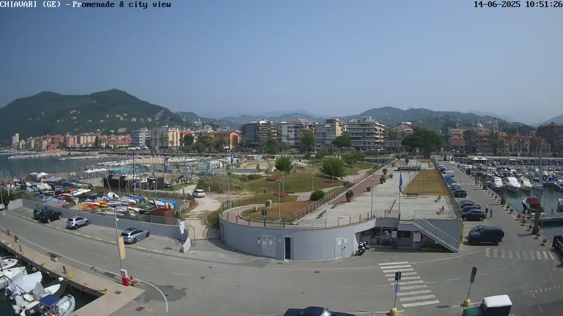 A sunny day overlooking a harbor filled with boats, a promenade, and a city nestled against a hillside.