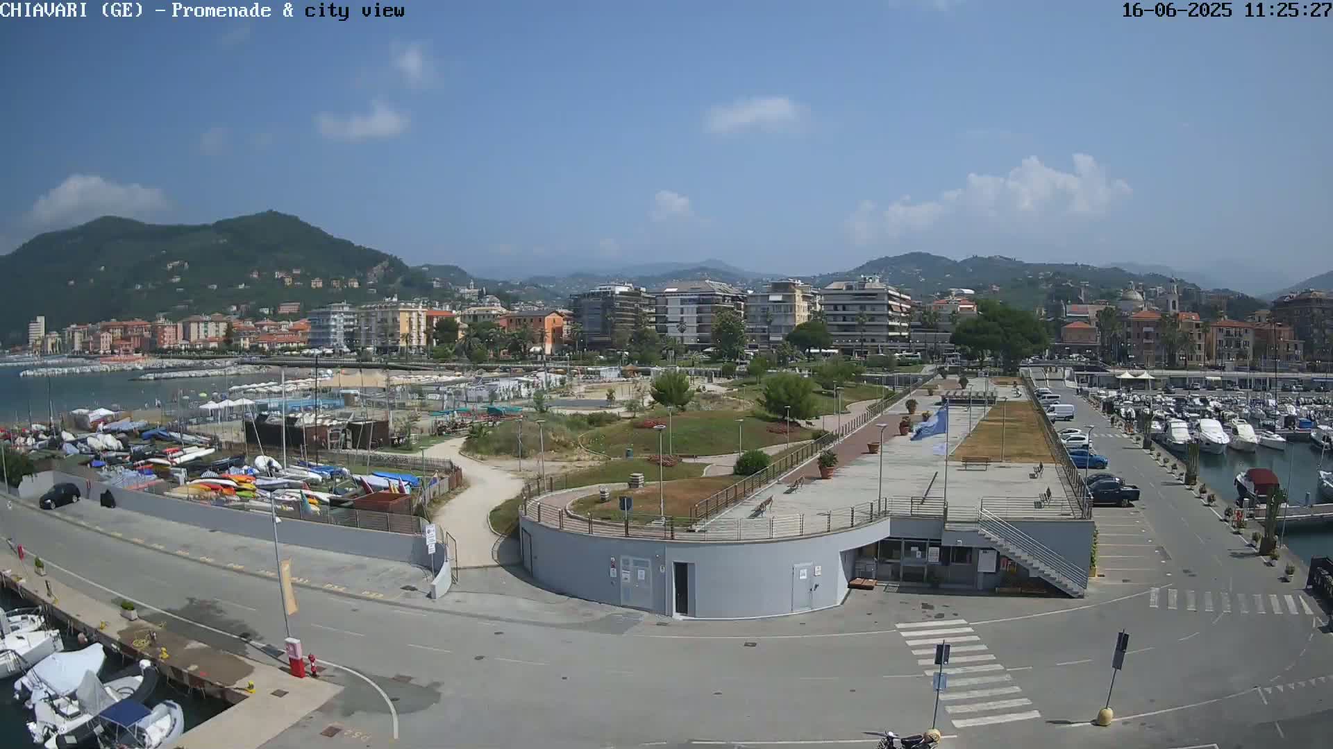 A coastal city with a marina and promenade is shown on a sunny day, with mountains in the background.