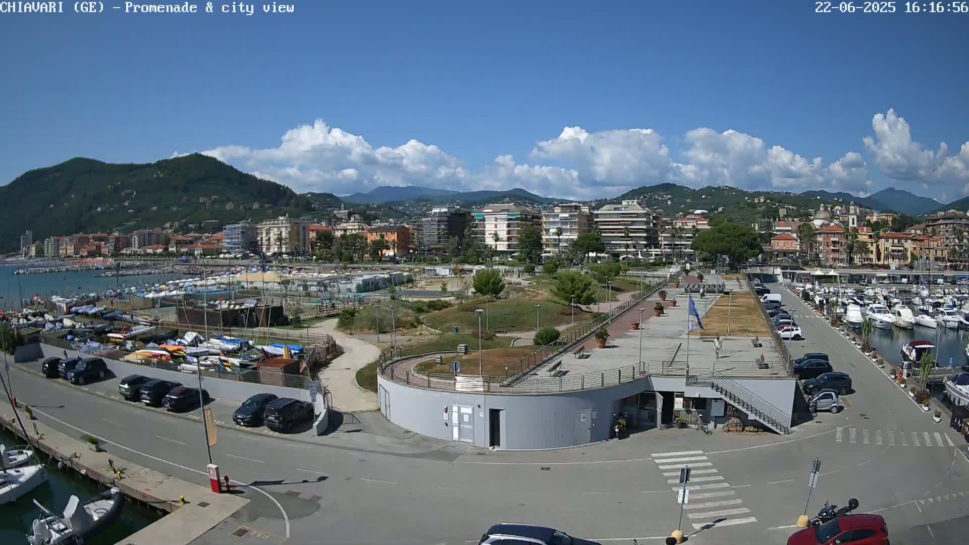 A coastal city with a marina and promenade is seen under a partly cloudy blue sky.