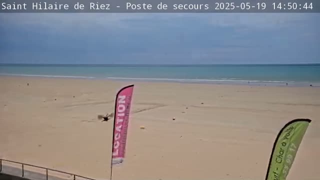 A mostly sunny beach with a calm ocean and a few people sparsely scattered across the sand.