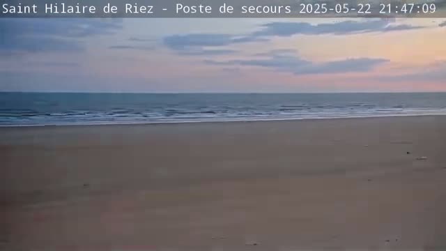A wide, sandy beach stretches to a calm ocean under a twilight sky.