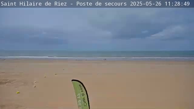 A wide sandy beach stretches to a calm ocean under a mostly cloudy sky.