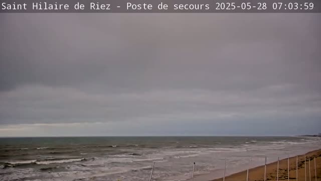 A grey, overcast sky hangs over a beach with moderate waves rolling onto the shore.