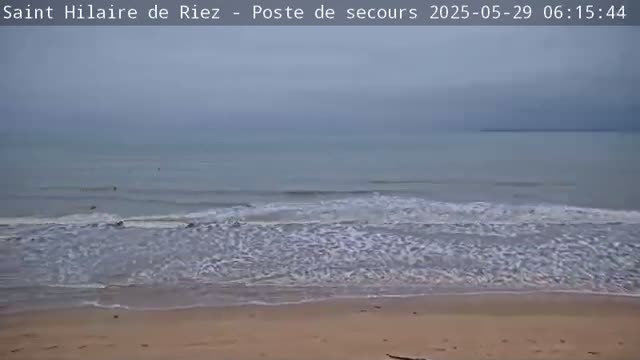 A sandy beach with gently rolling waves under an overcast sky.