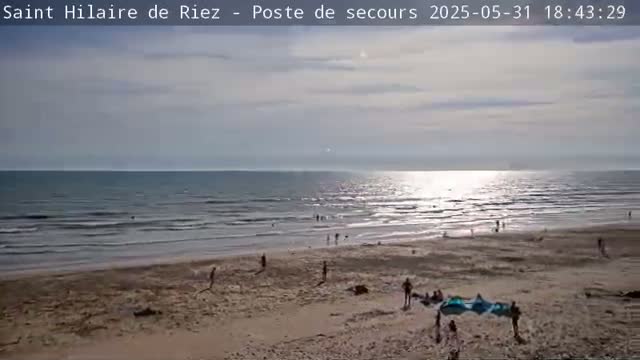 A mostly sunny day shows a beach with a few people scattered across the sand and in the ocean under a partly cloudy sky.