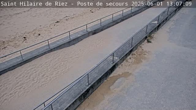 Two concrete ramps with metal railings descend to a sandy beach, where water appears to be partially covering the sand.