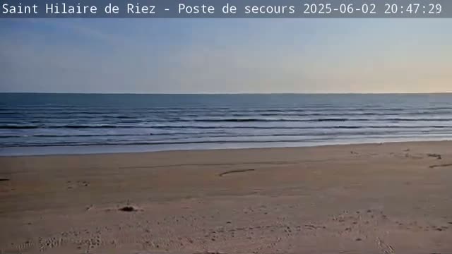 A sandy beach stretches to a calm ocean under a clear, pale sky.
