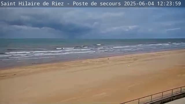 A wide sandy beach stretches out to a calm ocean under a mostly cloudy sky.