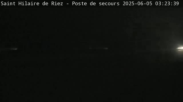 A dark, nighttime outdoor scene shows a faint light source on the horizon.