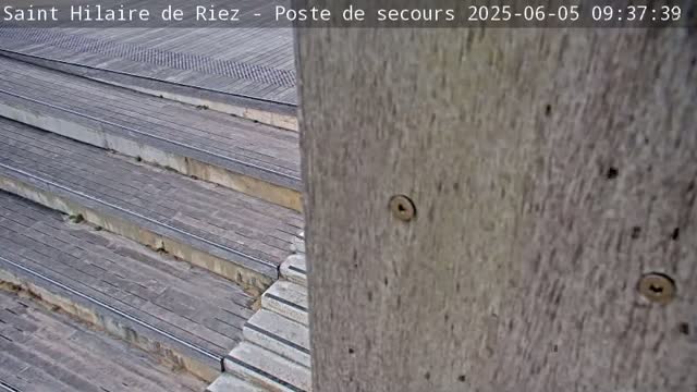 A view of wooden outdoor stairs leading down, partially obscured by a weathered grey wooden post.