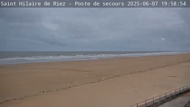 A wide shot of a sandy beach with gentle waves under a cloudy sky.