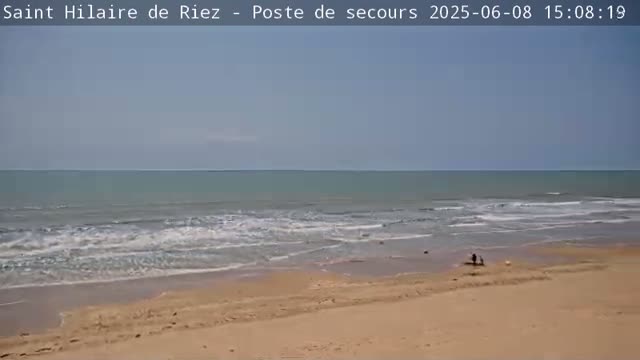 A sandy beach with gentle waves under a clear, light-blue sky.