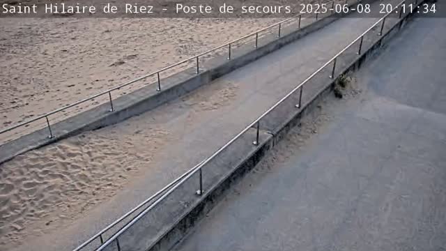 A paved walkway with metal railings slopes down to a sandy beach.