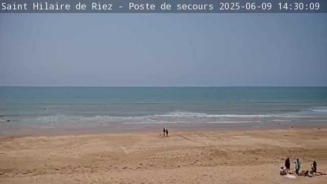 A sandy beach slopes down to a calm, light-blue ocean under a clear sky.