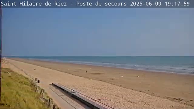 A long sandy beach stretches to a calm ocean under a clear blue sky.