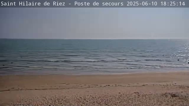 A sandy beach slopes down to a calm ocean under a clear sky.