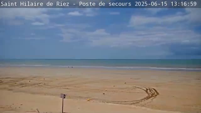 A mostly sunny day shows a wide sandy beach and calm ocean under a partly cloudy sky.