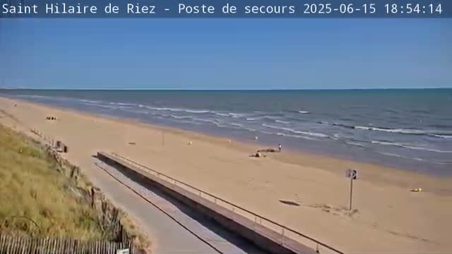 A sandy beach with a few people and a calm ocean under a clear blue sky.