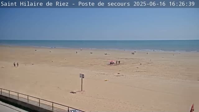 A mostly empty sandy beach stretches to a calm ocean under a clear blue sky.